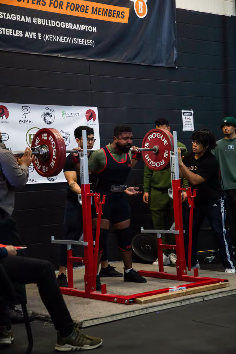 Vithusan J spotting a lifter through a heavy barbell squat at a Toronto strength competition