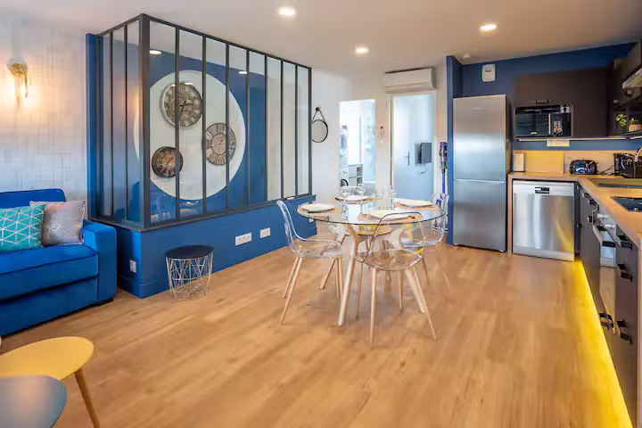 Appartement de 70 m² rénové : séjour ouvert avec cuisine bleu nuit, table à manger, séparation en verre et métal noir et parquet en bois clair