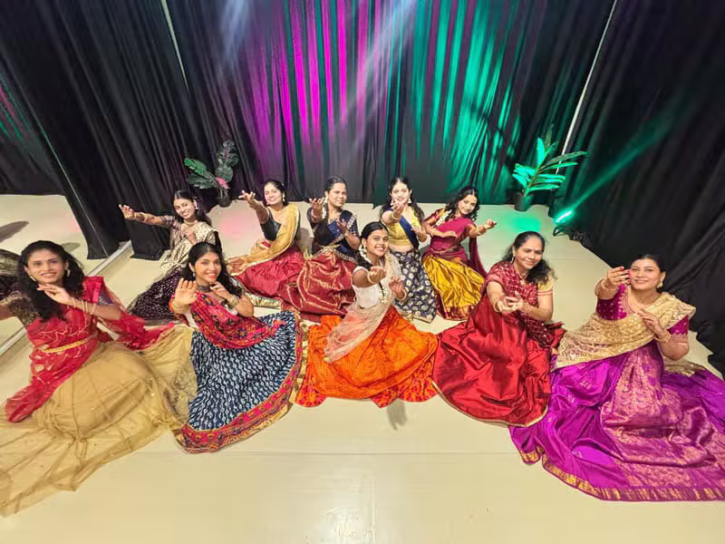 Dancers in costume seated on stage under colourful lights