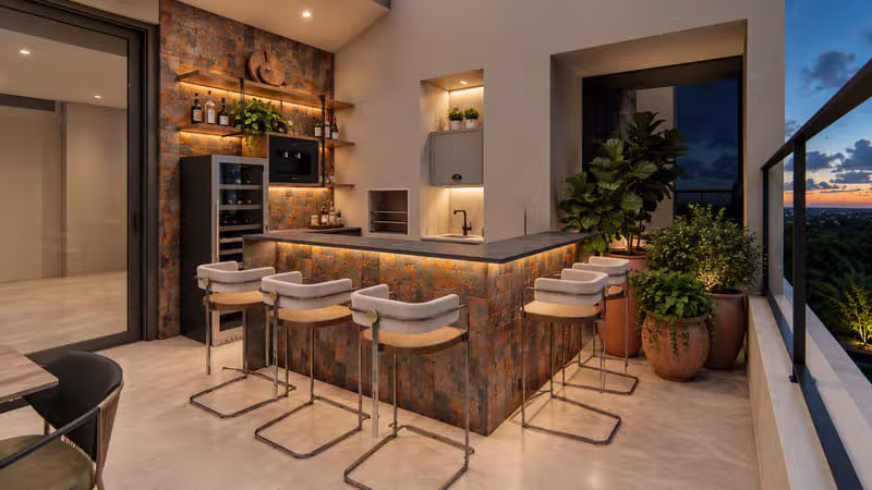 Varanda gourmet de apartamento com adega, bancada iluminada e vista para o pôr do sol