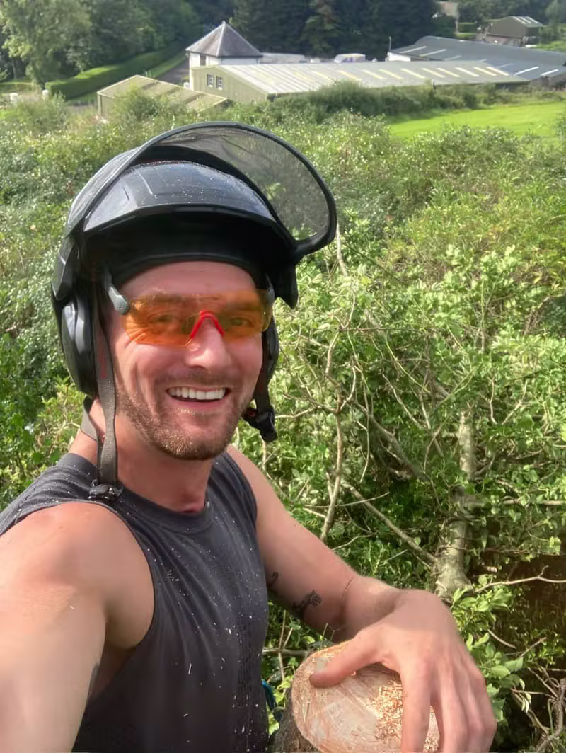 Tree surgeon in a safety helmet and tinted glasses beside freshly cut timber