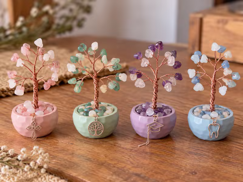 Cuatro mini arbolitos de la vida con dijes delicados —cruz de filigrana, árbol de la vida, birrete y diente— en cuencos pastel de cerámica