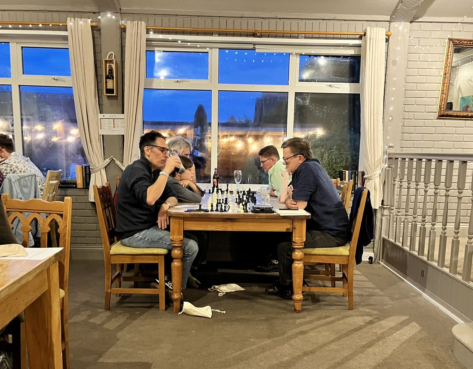 Players concentrating on games at a long table beside the windows in the Garden Room.