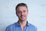 Australian mathematician Geordie Williamson in front of a white board.