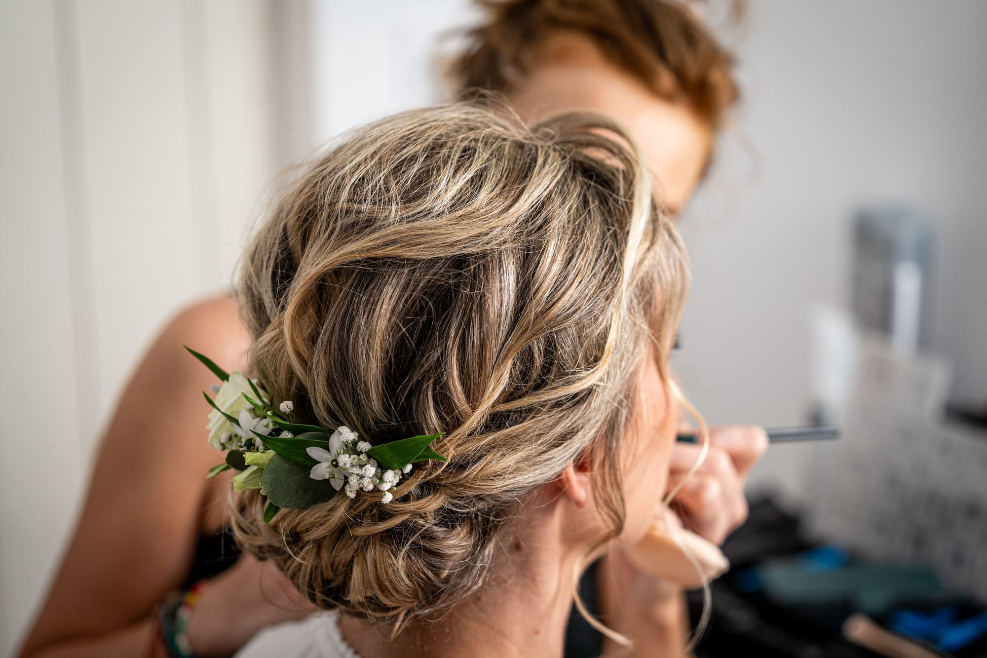 Mariée chignon ondulé avec fleurs naturelles, boucles souples autour du visage, maquillage naturel tons chauds