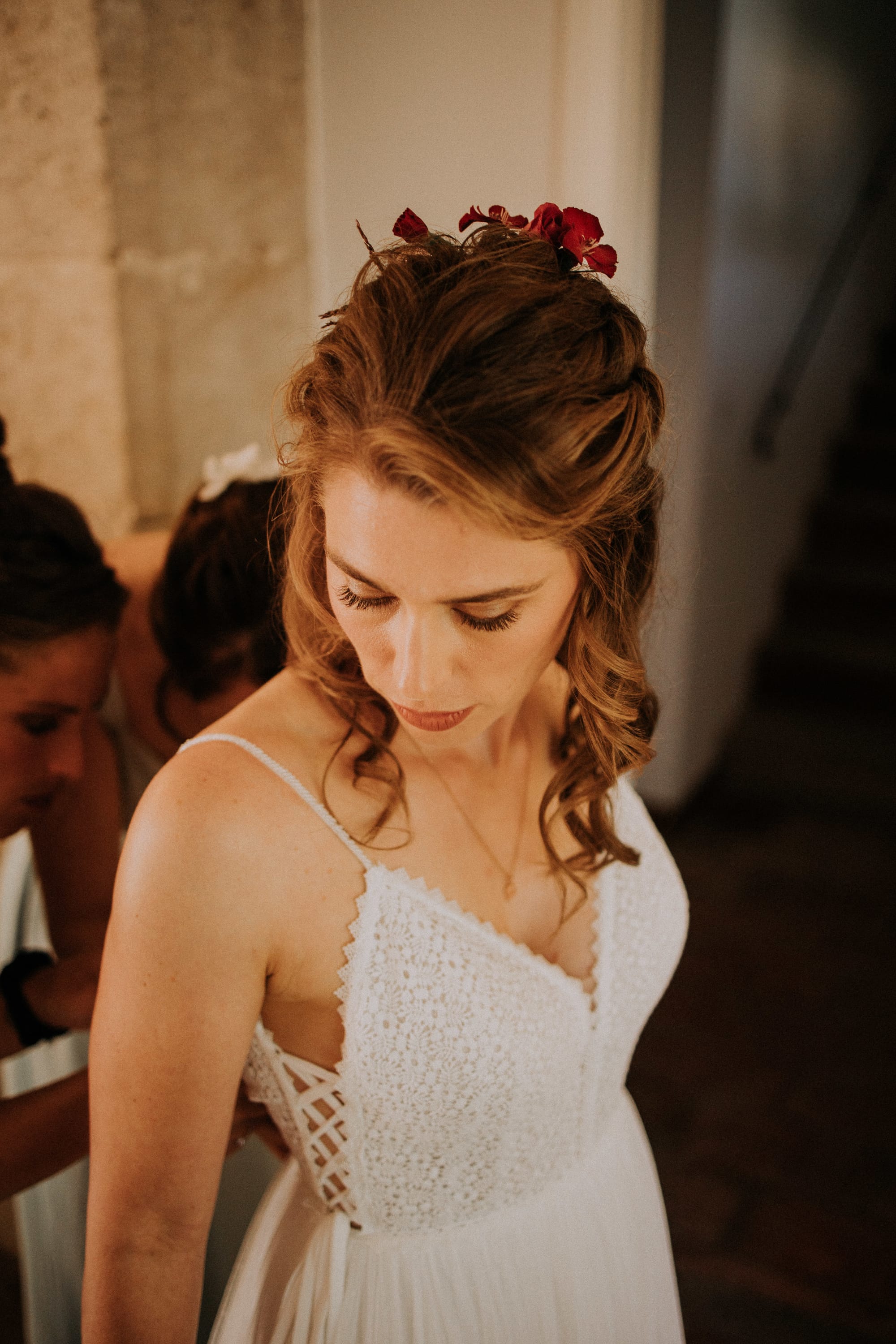 Mariée robe guipure à bretelles, coiffure cheveux longs et bouclés fleurs rouges dans les cheveux