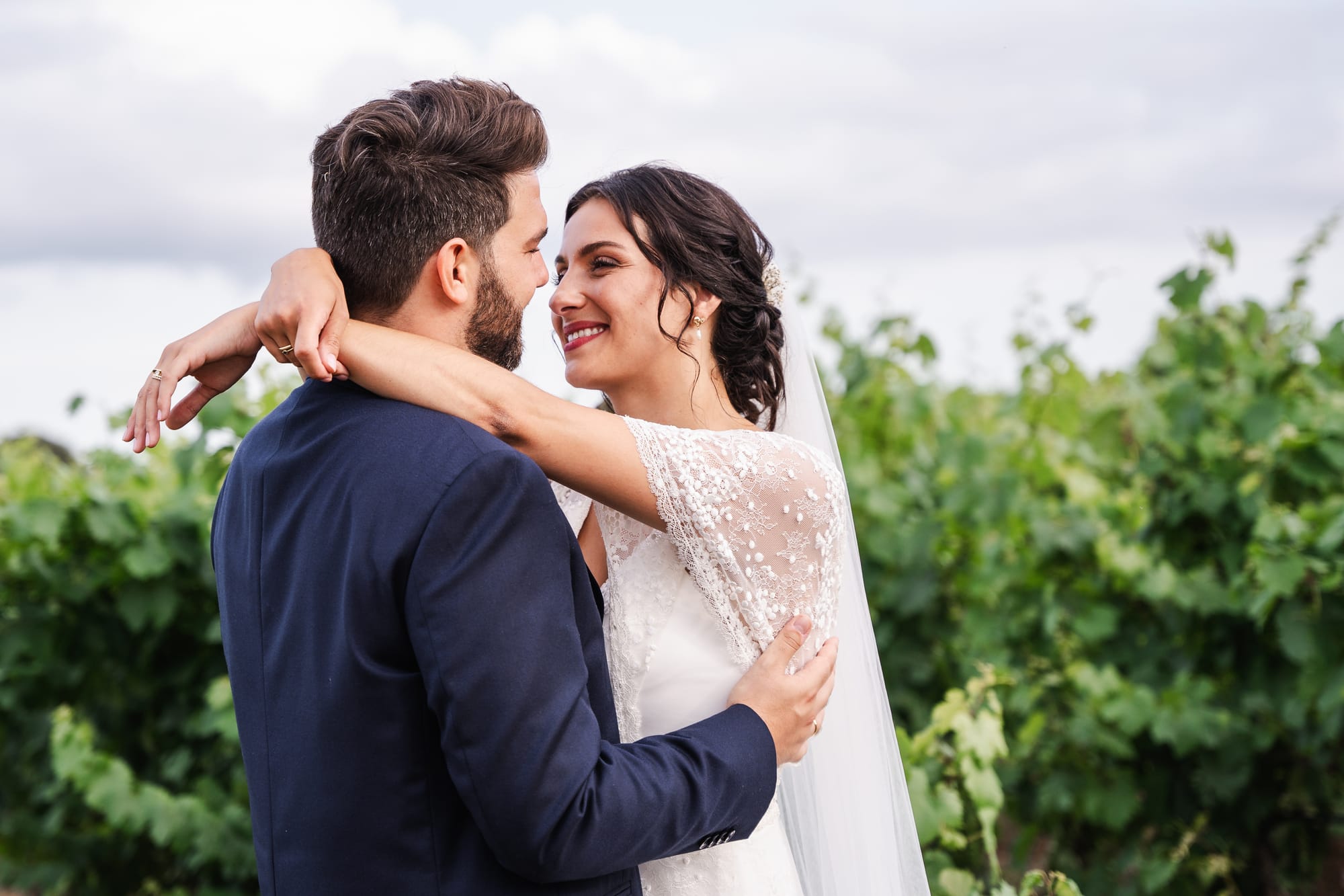 Robe de mariée avec petites manches en dentelles, chignon bas, boucles souples autour du visage avec voile et fleurs séchées