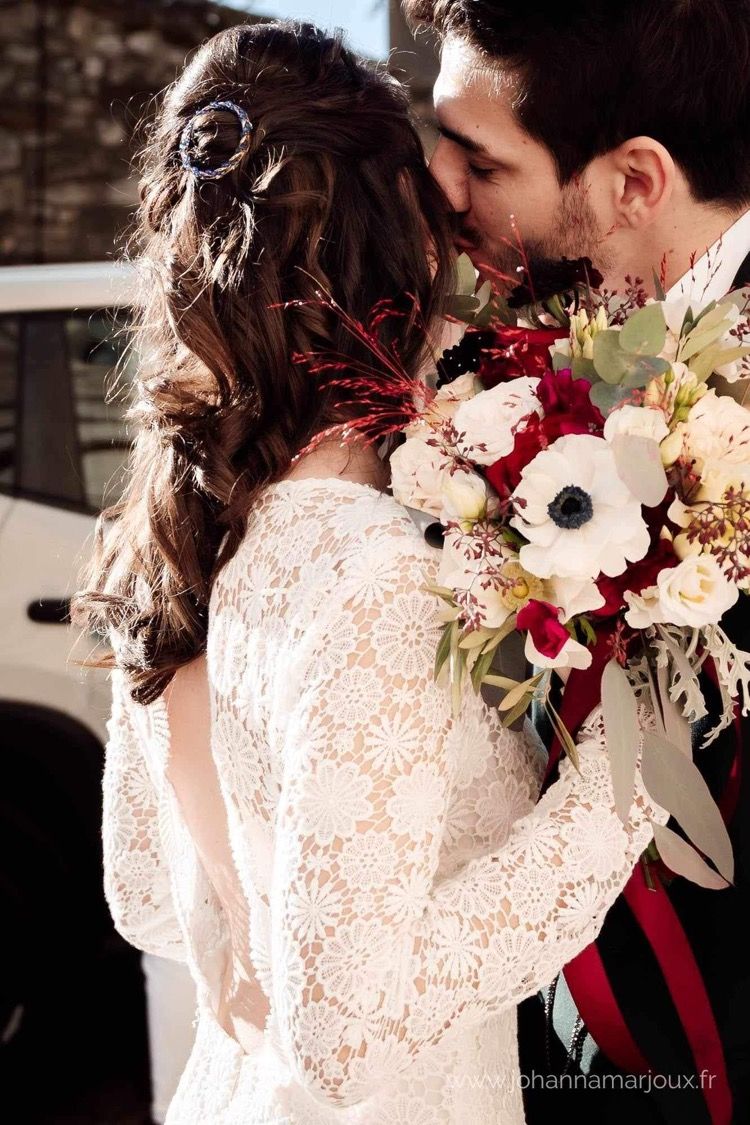 Mariée robe dentelle, cheveux long naturels bouclés avec barrette, bouquet fleurs blanches, rouges