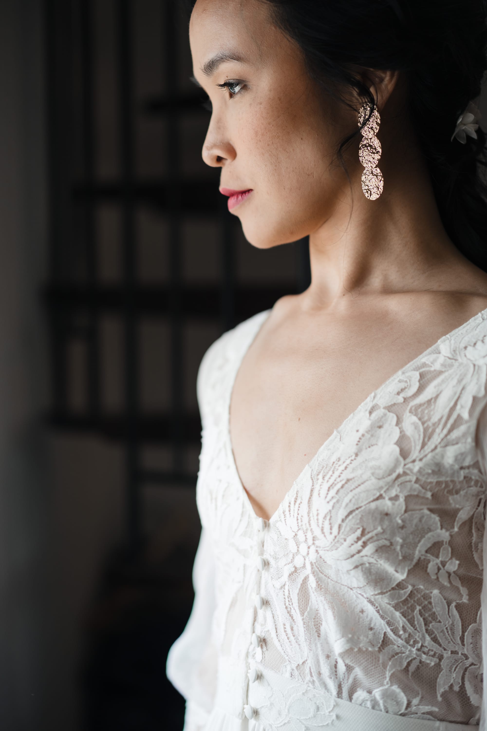 Mariée de profil, boucles d'oreilles pendantes dorées, robe de mariée en dentelle