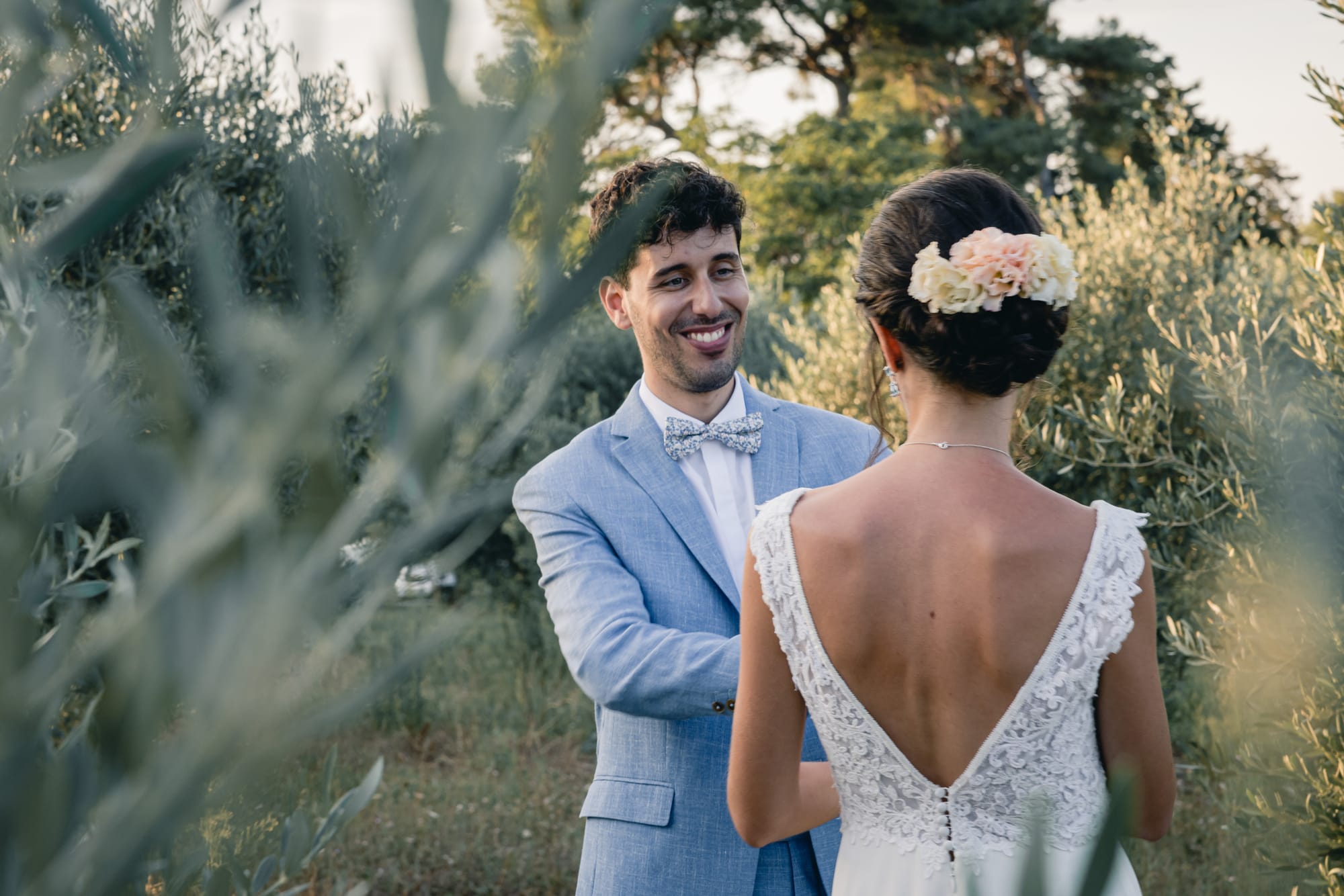 Coiffure de mariée, chignon bas avec roses naturelles, robe dos nu décolleté en V dentelle