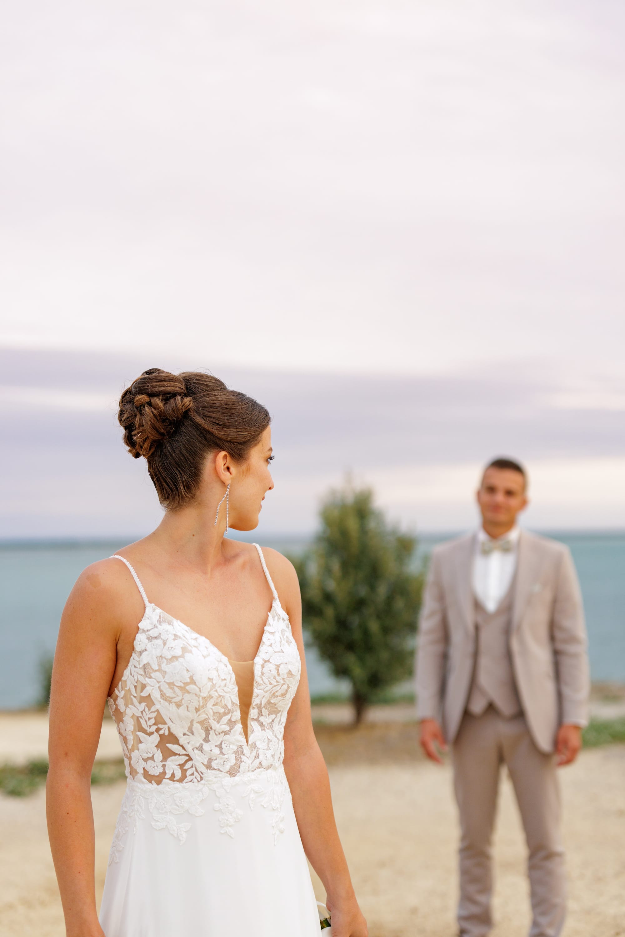 Coiffure de mariage chignon haut avec mèches torsadées, boucles d'oreilles strass, robe bustier dentelle
