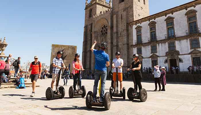 Tourists enjoying a Segway tour in Porto, standing on their Segways in front of a historic church in a lively city square.