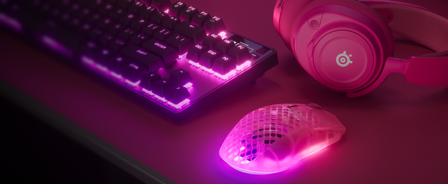 Image of mouse, mousepad and headset in magenta pink alongside keyboard with pink RGB glow