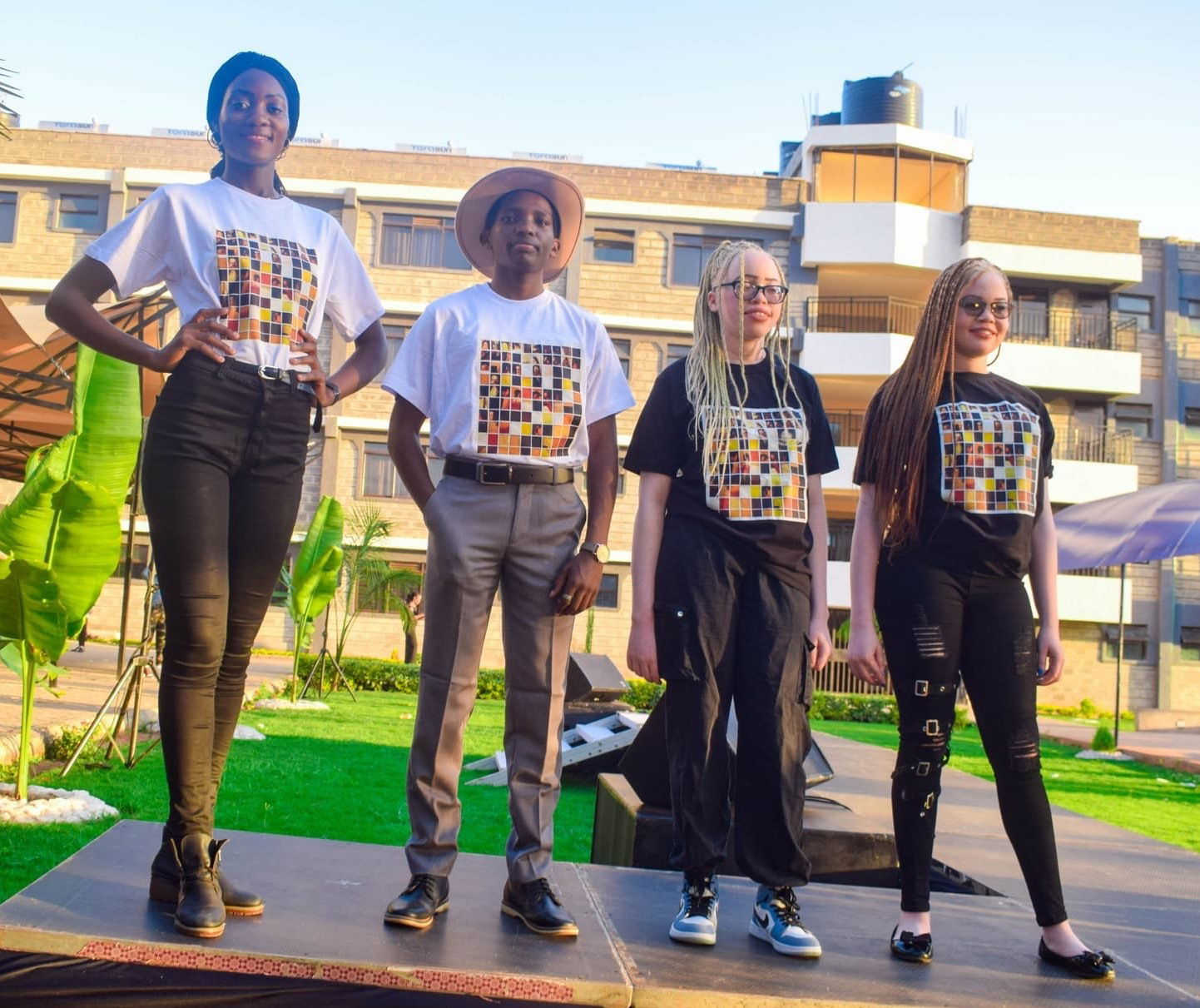 A group of four people stand on a podium showcasing apparel from black albinism. Two are persons with albinism and tow aren't 