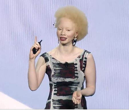 A picture of Thando Hopa dressed in a dress talking to people