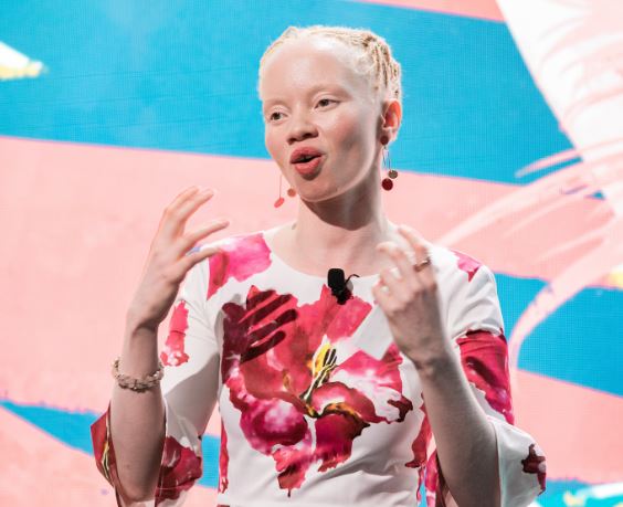 A picture of Thando Hopa in a colourful dress talking to people from a stage