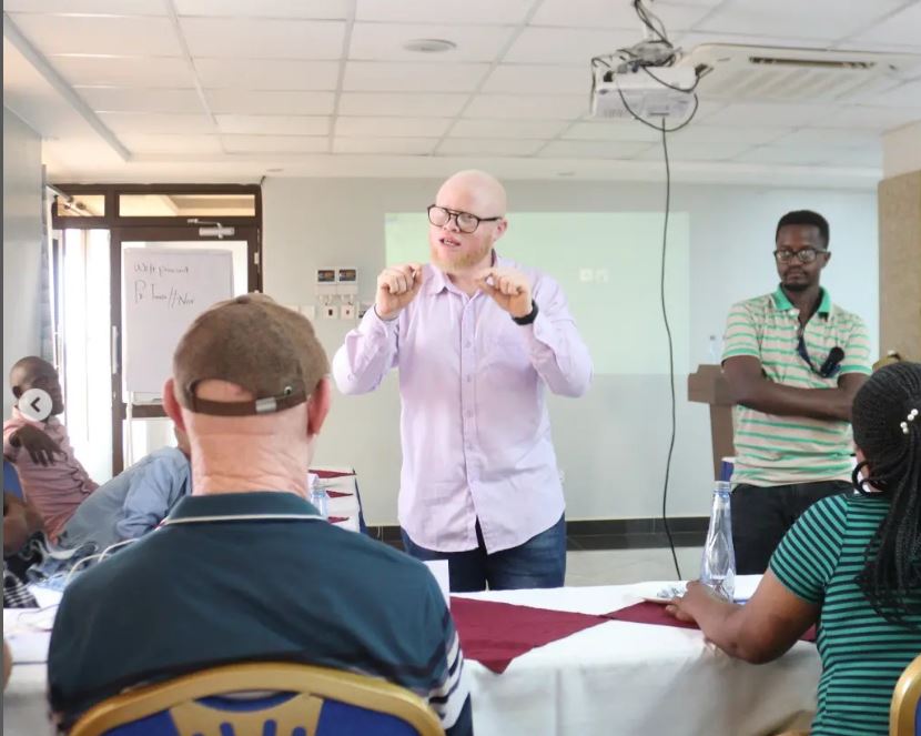 A picture of our Executive Director Alan Herbert explaining a point to peesons with albinism, next to him is our Access tp Government Opportunities Facilitator Morris Kinywa in a green T-shirt. All of them are facing the participants