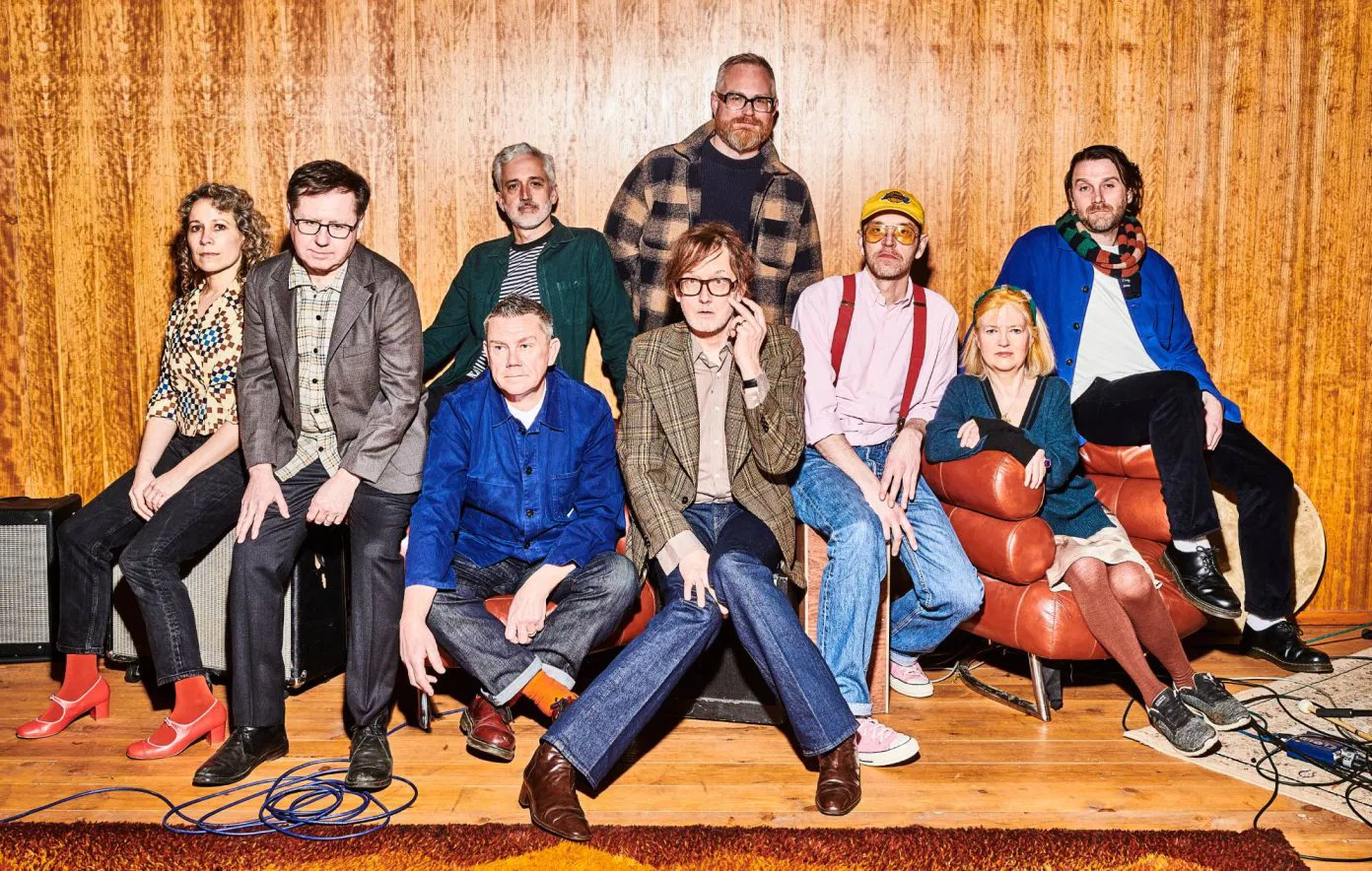 Members of the Britpop band Pulp stand together in a group portrait from their 2025 reunion tour, celebrating the release of More, their first new album in 24 years. From left to right, the members are:  Mark Webber (guitar)  Candida Doyle (keyboards)  Jarvis Cocker (lead vocals)  Nick Banks (drums)  The 2025 iteration of the band also includes touring members such as bassist Andrew McKinney, violinist Emma Smith, and multi-instrumentalist Adam Betts, who supported the core lineup during their sold-out arena tour and secret Glastonbury performance. The band dedicated this new era and album to their late long-time bassist, Steve Mackey, who passed away in 2023.