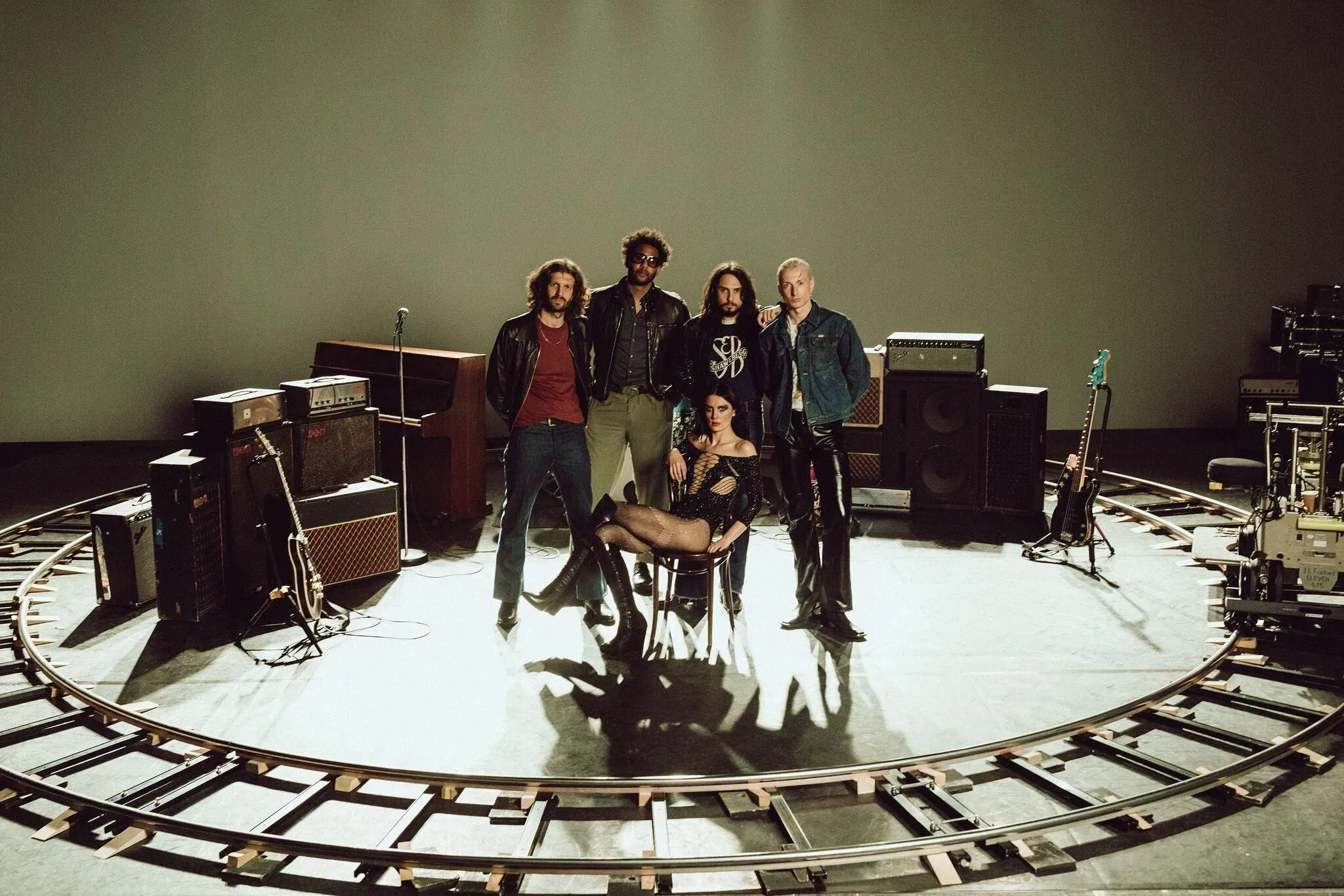 Members of the rock band Wolf Alice are captured on stage during their 2025 "The Clearing" arena tour, performing in front of a giant starship-silver metallic fringed curtain. From left to right, the members include Theo Ellis (bass), Joff Oddie (guitar), Ellie Rowsell (lead vocals/guitar), and Joel Amey (drums). The stage design for this tour features a high-impact, 1970s glam-rock aesthetic, complete with a massive tinsel backdrop and a large reflective silver star and disco ball that echo the visual themes of their fourth studio album, The Clearing. During their two-night homecoming residency at London’s O2 Arena in early December, the band delivered a career-defining setlist that ranged from cinematic ballads like "Thorns" and "The Last Man on Earth" to the chaotic punk energy of "Yuk Foo" and "Smile".