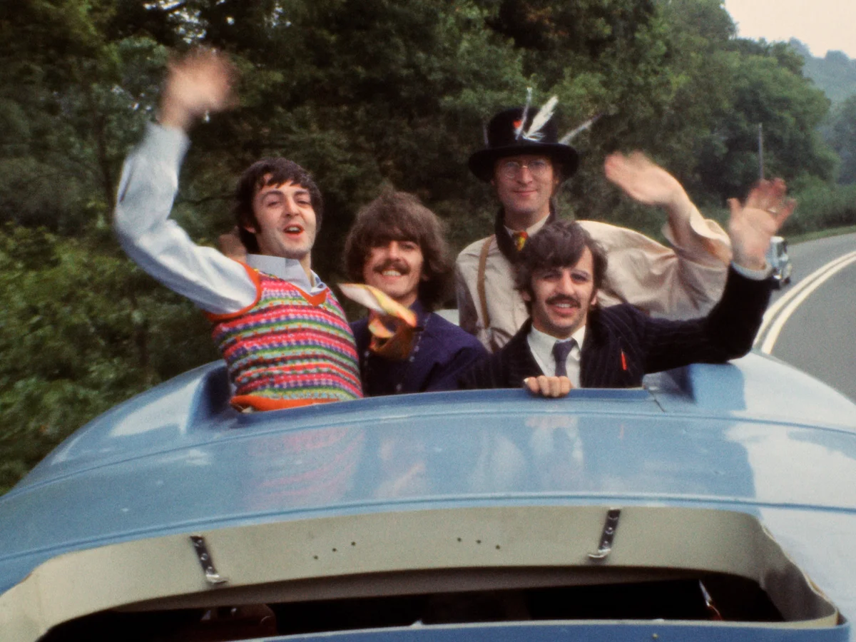 Members of the rock band The Beatles wave and cheer from the roof and windows of their brightly colored Magical Mystery Tour bus during the filming of their 1967 television special. From left to right on the upper deck, the group includes John Lennon, Paul McCartney, George Harrison, and Ringo Starr. The yellow and blue Bedford VAL coach features "Magical Mystery Tour" branding and carried the band, film crew, and various actors on an unscripted journey across the West Country of England. This iconic image captures the playful, psychedelic spirit of the era, which also produced the classic soundtrack album featuring tracks like "I Am the Walrus" and "The Fool on the Hill".