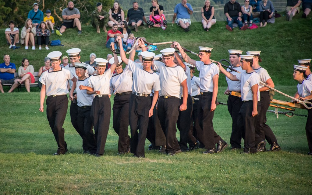 Un groupe de cadets de la Marine tenant une corde au-dessus de leur tête et portant leur gilet blanc et leur bonnet de marin.