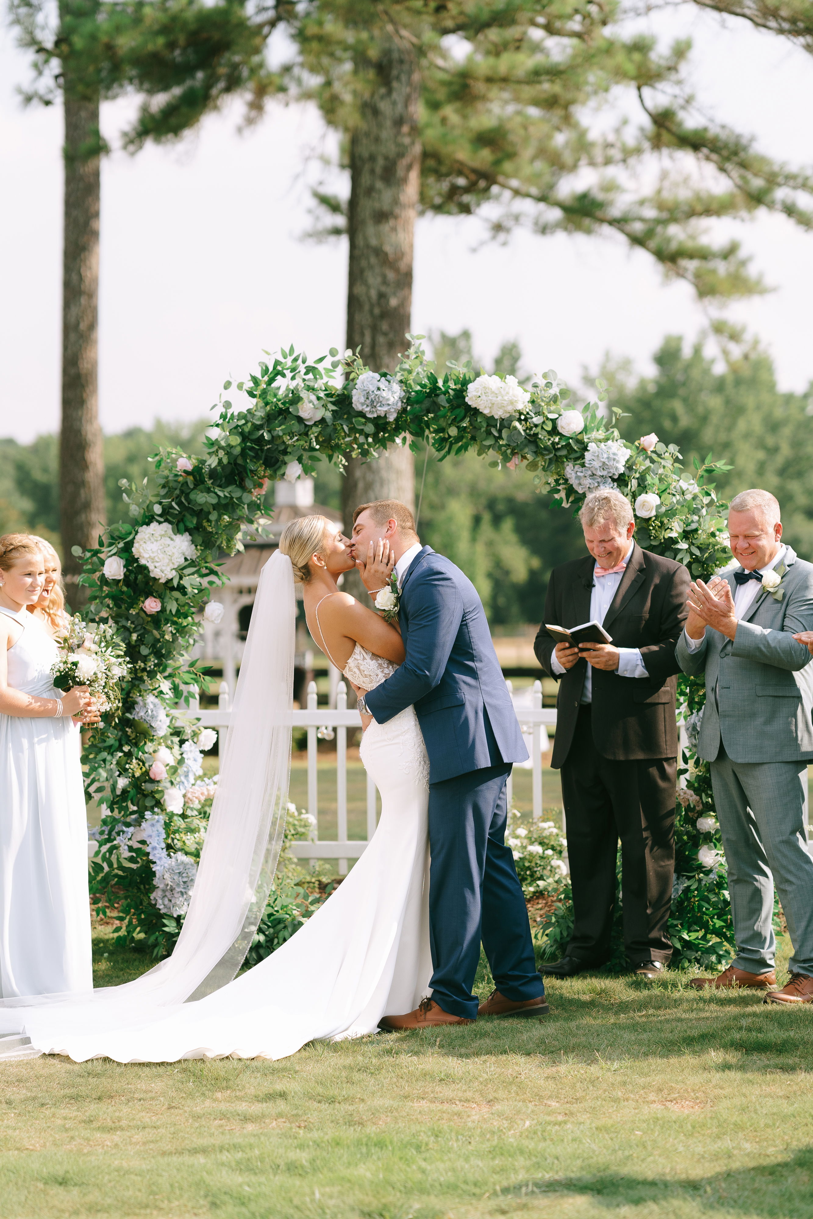 bride and groom first kiss in front of lush floral omega arch in garden setting of courtyard near Oconee County, GA 