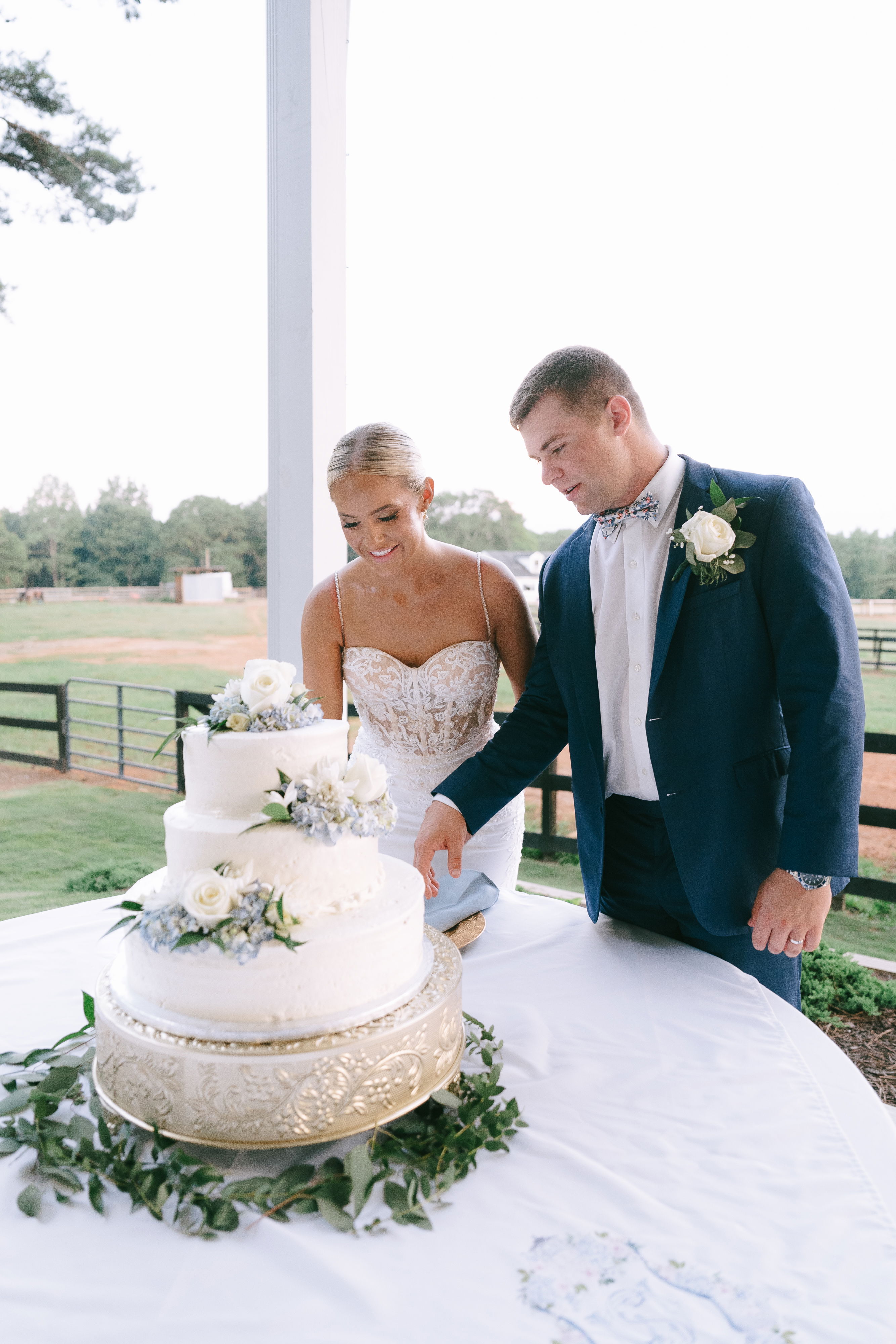 bride and groom in reception cutting wedding cake near field of horses and gazebo in Monroe, GA near Watkinsville, Georgia