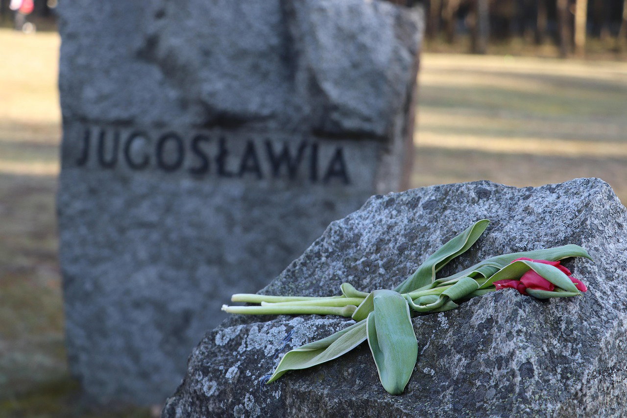 Una flor marchita sobre una piedra, cerca de una lápida con la leyenda Yogoslavia. Señal de la Guerra Fría. 