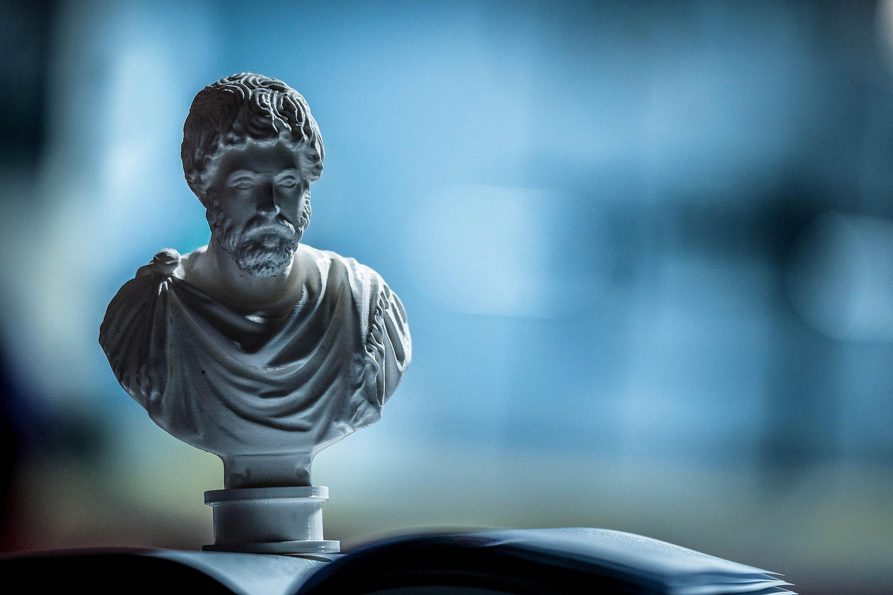 Pequeño busto de un personaje clásico en mármol sobre un libro, símbolo filosófico estoico de sabiduría.