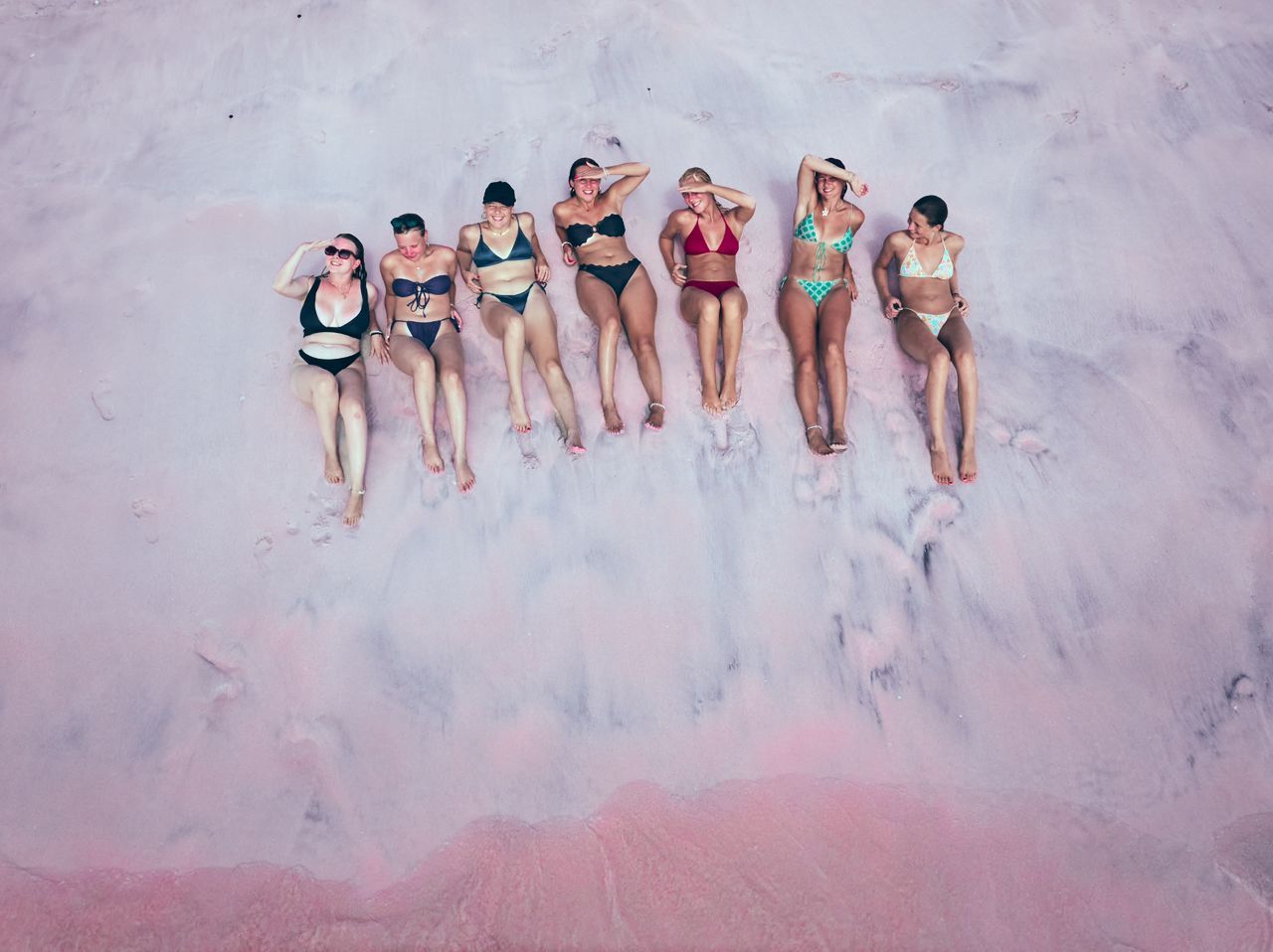 Group of people laying down in Pink Beach for drone moment