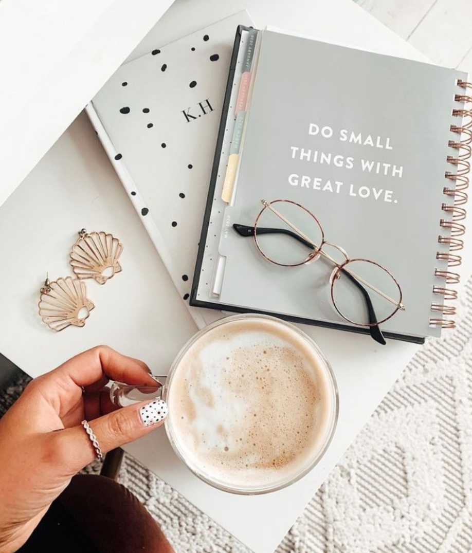 Hand holding a cup of coffee next to a notebook with glasses on top