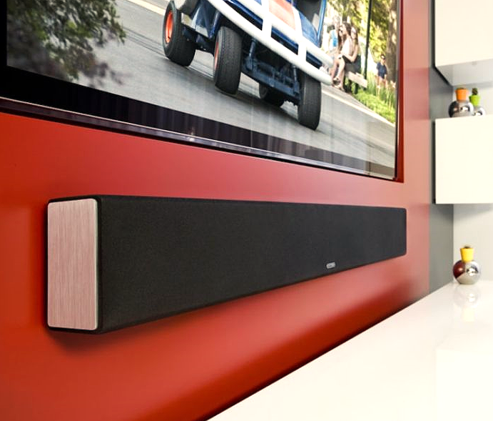 תמונת אווירה של ה Monitor Audio SB-4 סאונדבר תלוי על שידה לבנה ומעליו תלויה טלויזיה וקיר רקע בצבע אדום