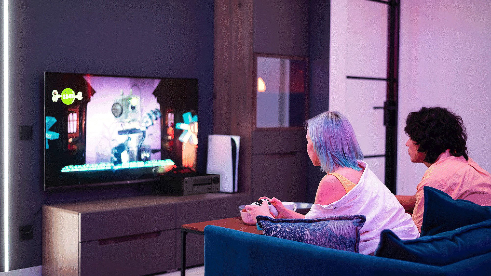 תמונת אווירה של נער ונערה משחקים Xbox בסלון מול טלויזיה גדולה ורסיבר Onkyo TX-NR7100 מונח מתחתיה 