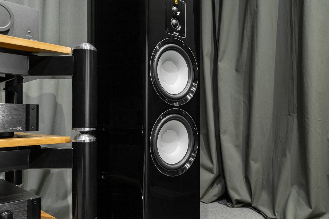תמונת אווירה של רמקול רצפתי Magnat Signature 909 בצבע שחור מבריק מונח על יד מערכת