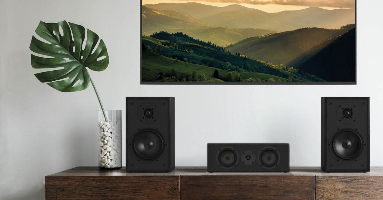  רמקול סנטר מגנט Magnat Monitor S12C יושב על שידה עם שני רמקולים מדפיים תואמים משני צידיו