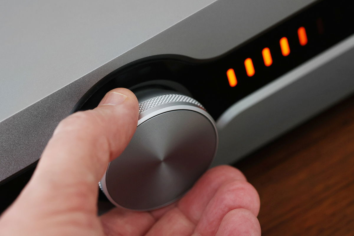 מגבר סטרימר Roksan Caspian 4G Streaming Amplifier בפוקוס על כפתור הווליום עם יד של מישהו שמזיזה אותו