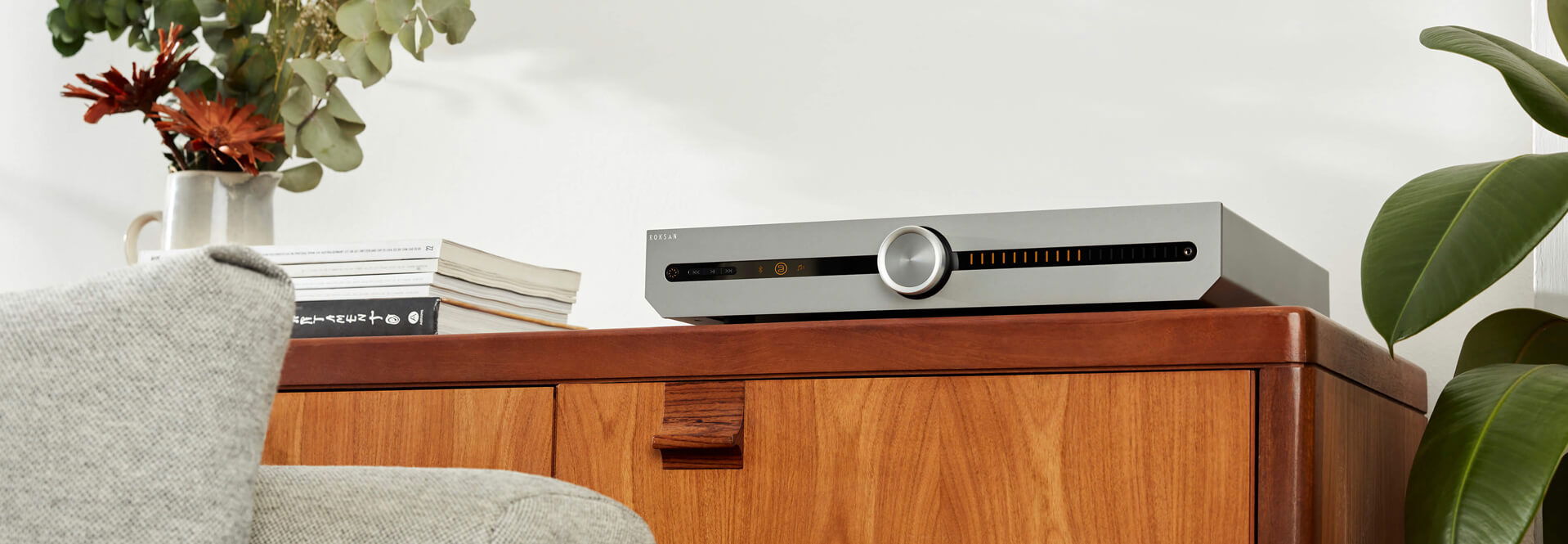 מגבר רוקסן Roksan Attessa Streaming Amplifier בצבע כסוף מונח על שידת עץ בסלון