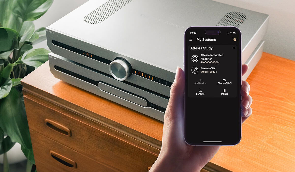 מגבר ונגן דיסקים רוקסן אטסה Roksan Attessa Streaming Amplifier מונחים אחד על השני על שידה ומישהו מפעיל אותם באמצעות אפליקציה