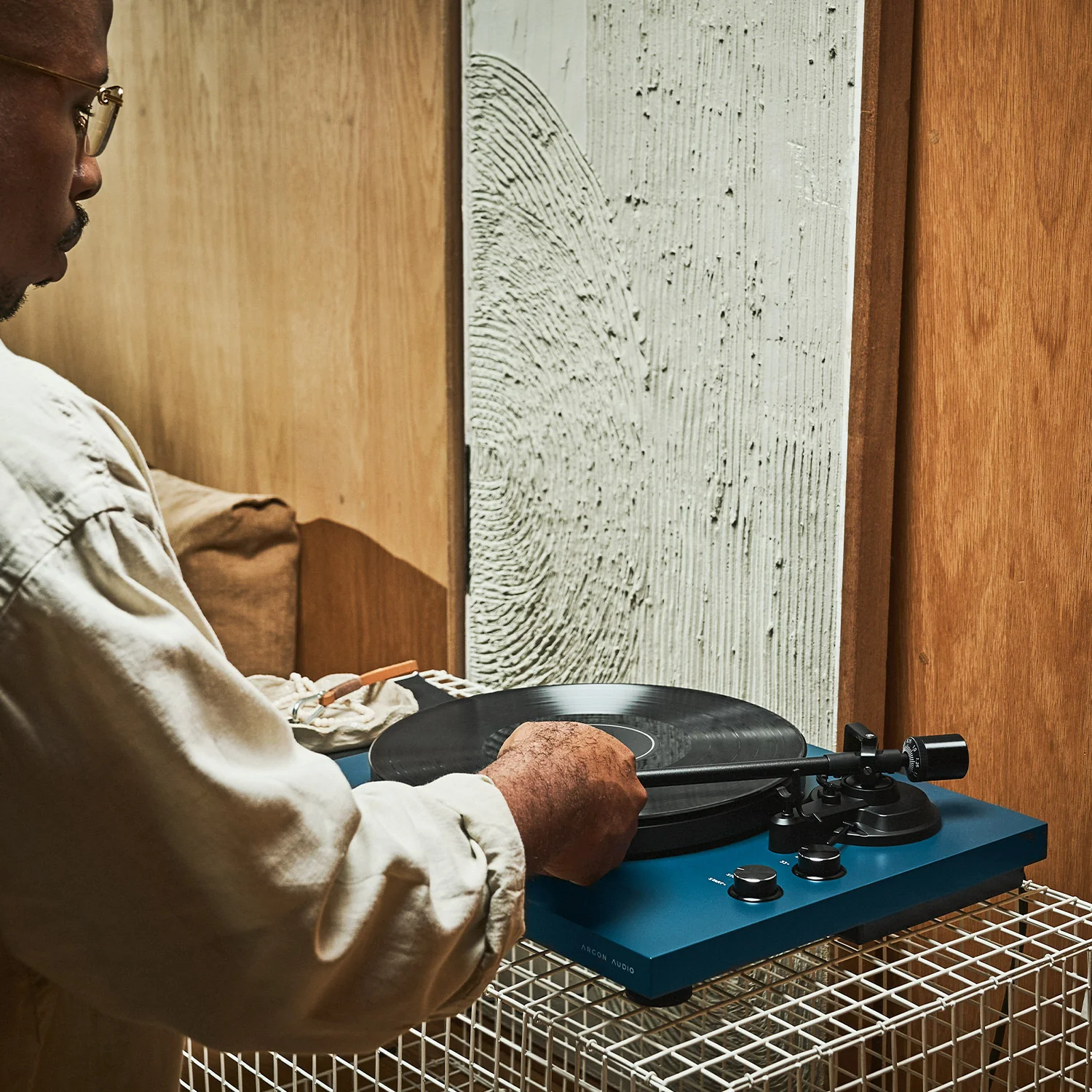 פטיפון ארגון Argon Audio TT MK2 בצבע כחול מונח על שיחדת ברזל ומישהו מפעיל אותו