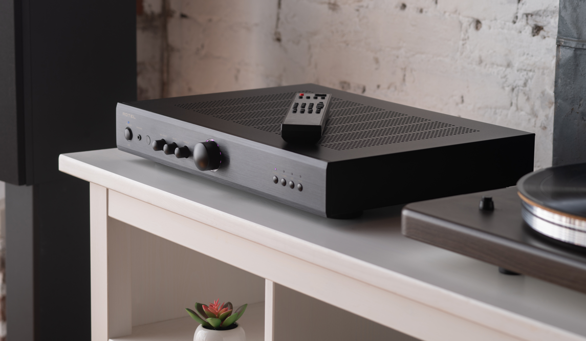 מגבר סטריאו משולב Rotel A8 בשחור עם שלט רחוק על שידת כניסה לבנה – מבט על כפתורי השליטה בעיצוב סלים דק ואלגנטי