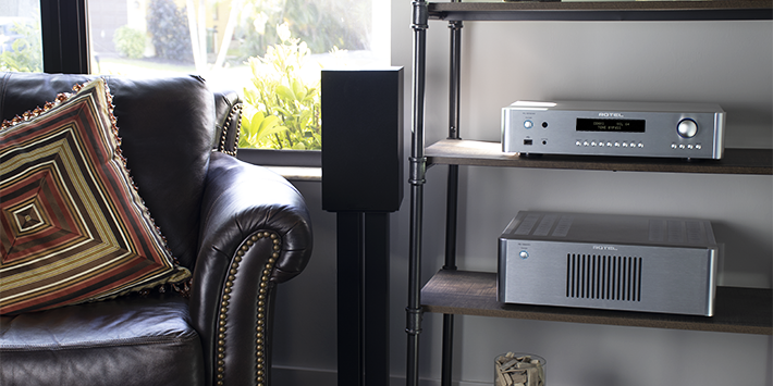 קדם-מגבר RC-1590MKII כסוף על מדף עליון לצד רמקול מדפי. עיצוב מינימליסטי עם צג טקסט כחול וחוגת ווליום מוארת