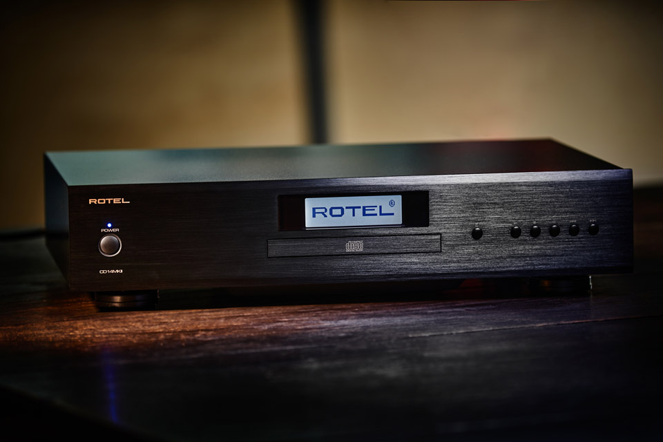 נגן Rotel CD14MKII בגימור שחור מוברש על משטח עץ. חזית אלגנטית הכוללת צג דיגיטלי מרכזי עם לוגו המותג ותאורת הפעלה כחולה