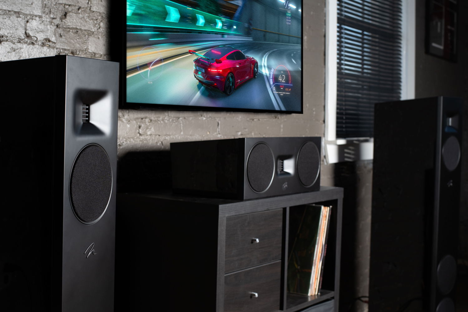 חווית קולנוע ביתי עם רמקולים רצפתיים Martin Logan Motion F10 ורמקול סנטר Motion C10 מסביב למסך המציג משחק מירוצים