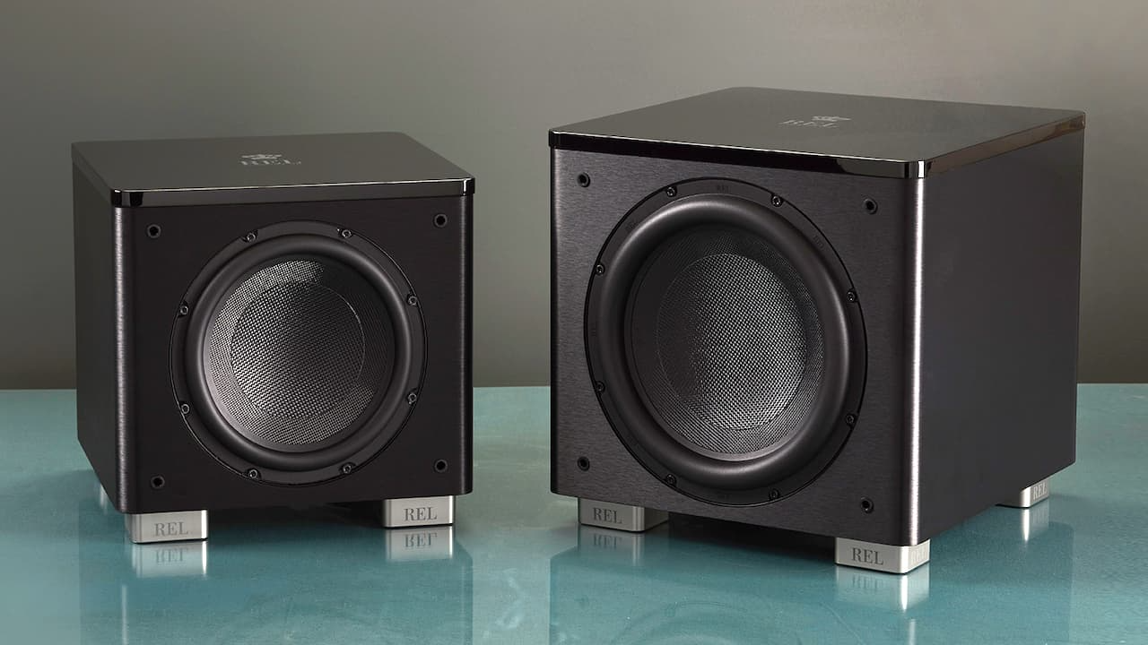 שני סאבים של רל REL HT/1003 MKII,REL HT/1205 MKII מונחים אחד על יד השני עם הטייה טיפה כלפי פנים על רקע תכלת