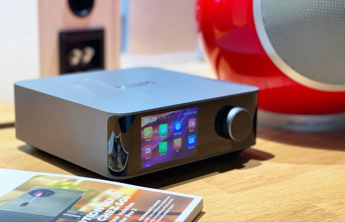 מגבר סטריאו סטרימר ווים WiiM Amp Ultra מונח על מדף על יד רמקול אדום מעוצב ועל יד מגזינים
