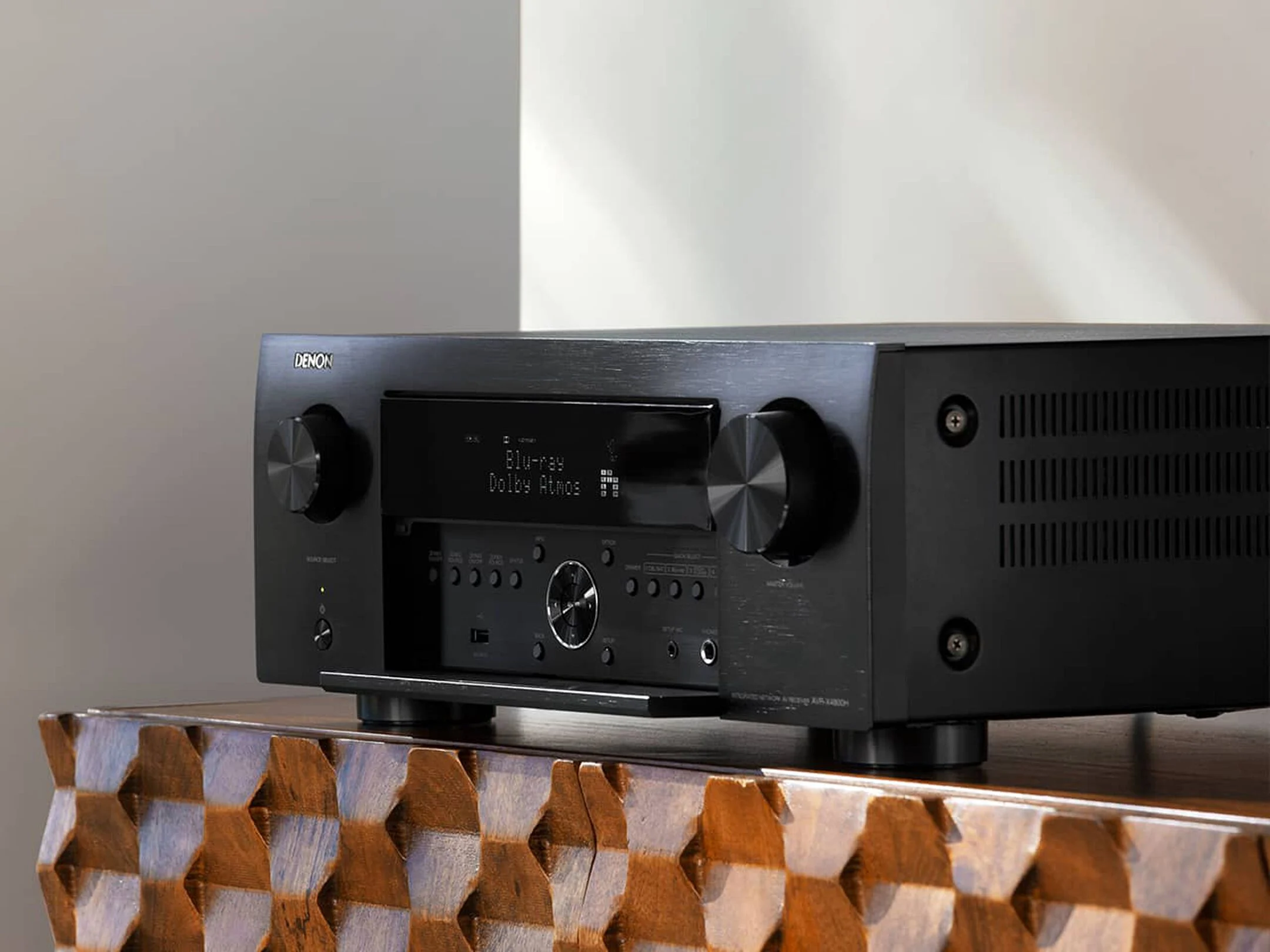 מגבר קולנוע ביתי דנון Denon AVC-X4800H עומד על שידת עץ מעוצבת בצילום זוויתי