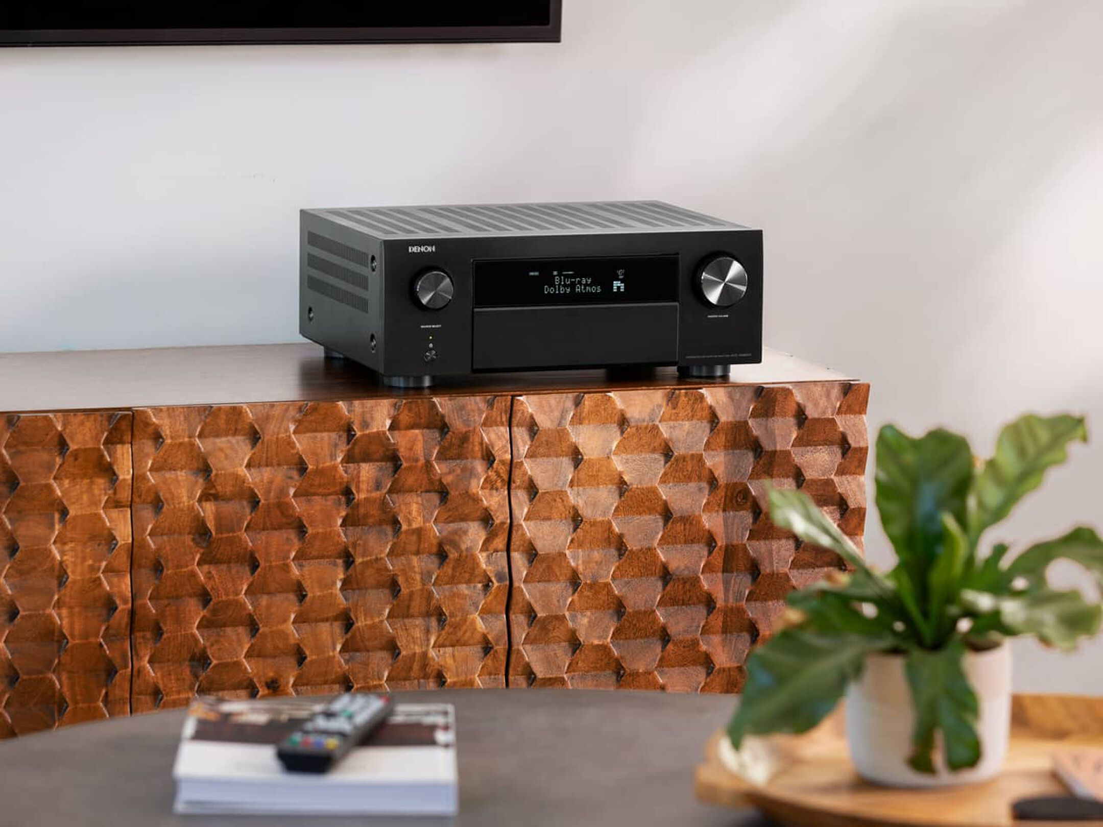 מגבר קולנוע ביתי דנון Denon AVC-X4800H עומד על שידת עץ מעוצבת בצילום חזיתי