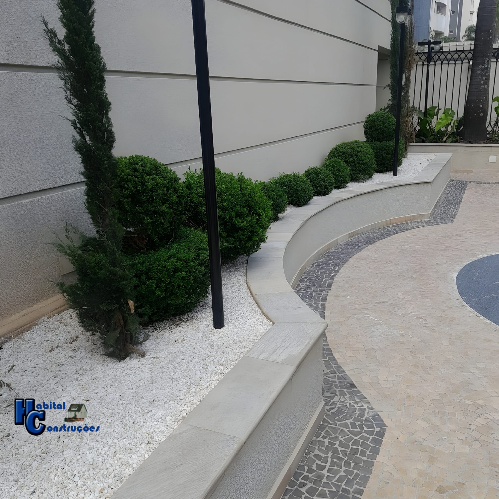 O ambiente é marcado por um paisagismo com plantas de baixo porte. Há uma variedade de arbustos, alguns com formato esférico.