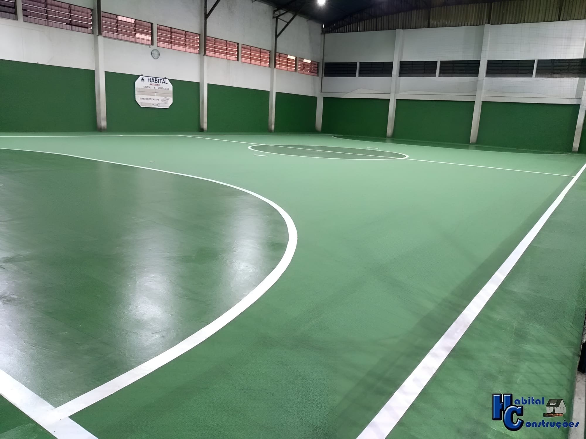 Quadra poliesportiva coberta, com piso de cor verde e marcações em branco.