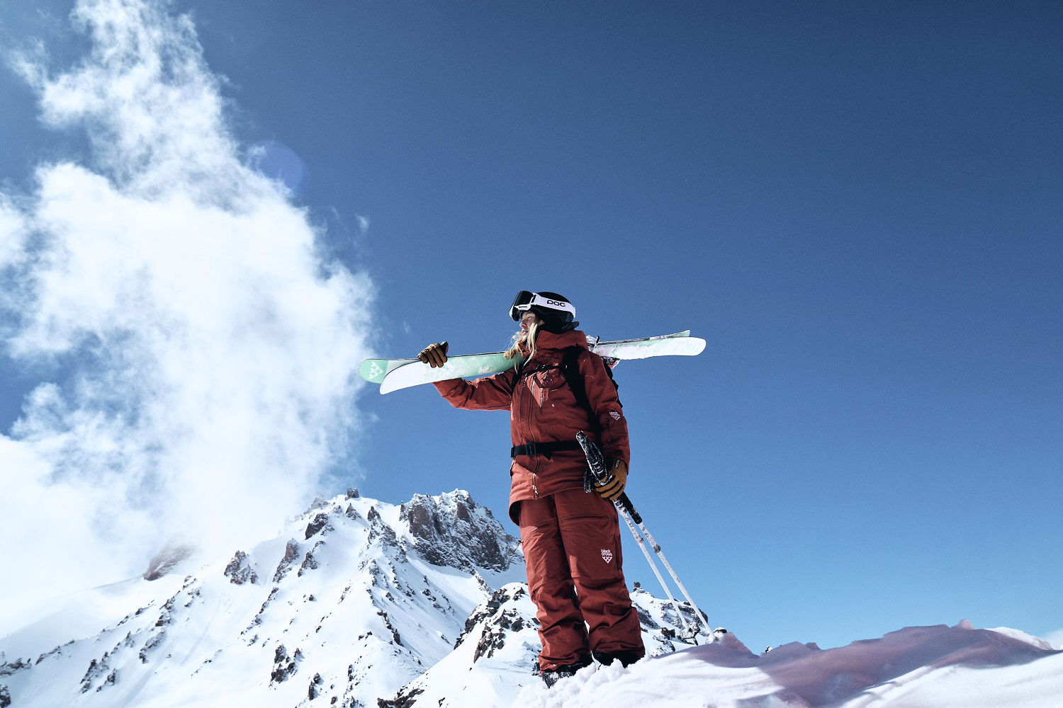 Person som står på toppen av et fjell med ski på skuldrene